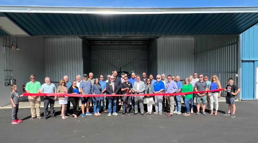 a crowd stands ready to cut the ribbon in front of the new t-hangars