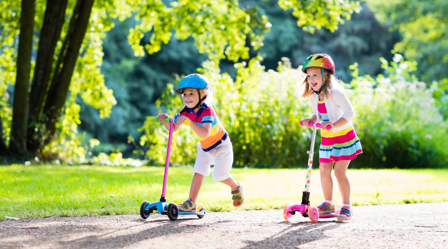 two young girls riding scooters in a park
