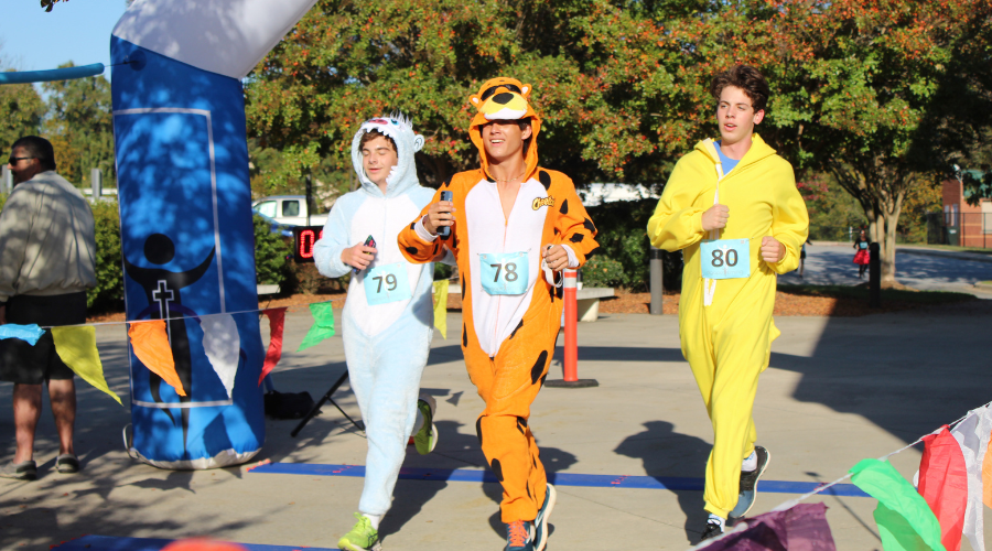 Three runners crossing finish line in Halloween costumes